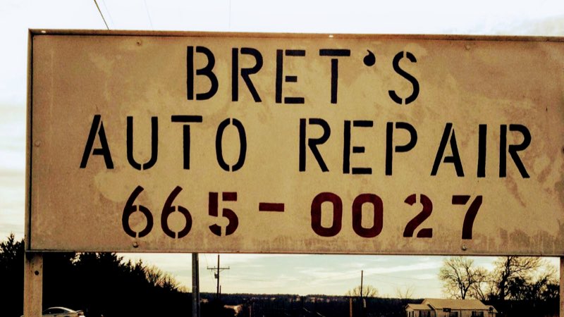 Bret's Auto Repair roadside sign, hand-stenciled with the shop name and phone number, against an Oklahoma sky